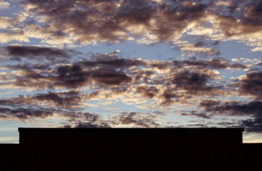 Çarpıcı menekşe, turuncu ve mavi gün batımı siyah bina silueti ve garip bulut oluşumları