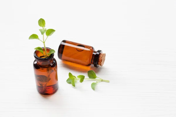 A bottle of oregano essential oil with fresh oregano leaves on w — Stock Photo, Image