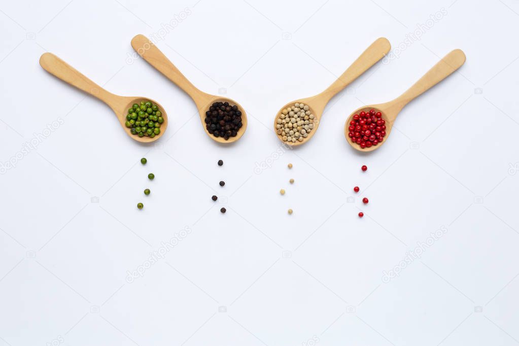 Green, red, white and black peppercorns with wooden spoon on whi