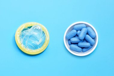 Condom with PrEP ( Pre-Exposure Prophylaxis) used to prevent HIV, in plastic pill bottle cap on blue background. Save sex concept.  clipart