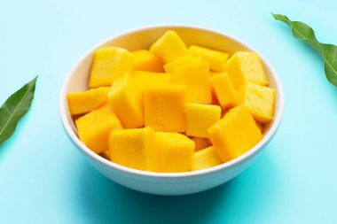 Tropikal meyve, mango küp dilimleri beyaz kasede mavi arka planda.