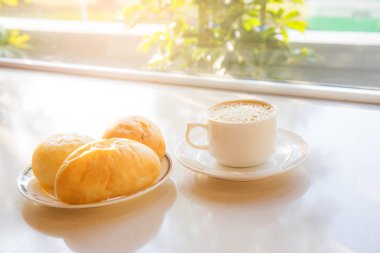 Beyaz kahve fincanı ba güneş ışığı ile masada ekmek ile