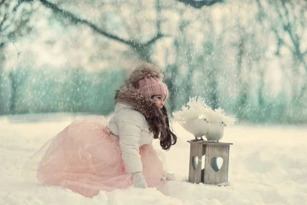 Inverno nevado e uma menina em um boné com pombas — Fotografia de Stock
