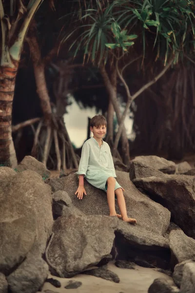 Under ett träd på en stor sten sitter en pojke — Stockfoto