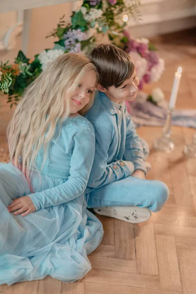 Kleine jongen en meisje in de blauwe jurk in de Studio met bloemen — Stockfoto