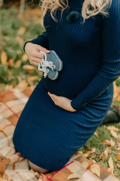 穿着蓝色连衣裙的女人拿着一双新生儿的鞋 — 图库照片