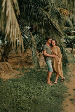 erkek ve kadın okyanus kıyısında palmiye ağaçları altında sarılma