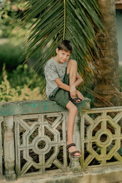 Der Junge Sitzt Auf Einem Zaun Unter Palmen — Stockfoto