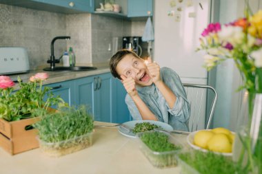 Mutfakta mikroyeşil tişörtlü bir çocuk.