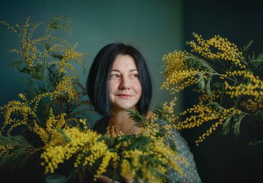 Baharda, çiçek açan bir bahçede, tulumlu bir kadın hasır sepetle poz veriyor.