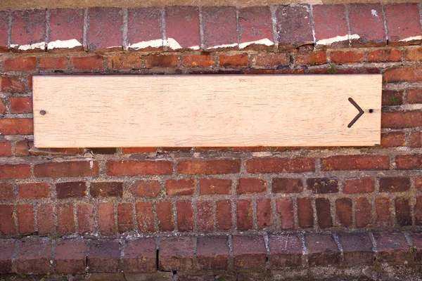 Wooden signpost with arrow on old brick wall