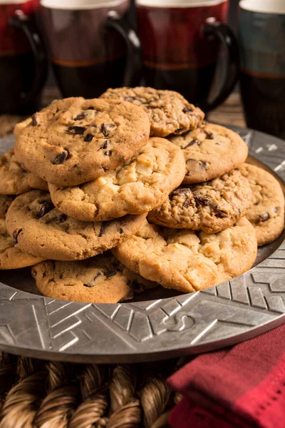 Çeşitli aromalı kurabiyelerden oluşan bir gruba yakın çekim. Çikolata parçacıklı, macadamia fındıklı, yulaf ezmeli kuru üzümlü, yemekten sonra servis edilen kahve fincanlarıyla gümüş bir tabakta veya atıştırmalık olarak.