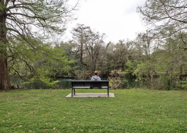 Bir kadın bankta oturmuş Audubon Park, New Orleans, Louisiana, ABD 'deki bir gölete bakıyor..