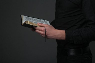 yüzü olmayan bir haç üzerinde gri bir arka plan ile bir rahip elinde açık bir İncil