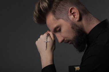 Rahip başı gri bir arka plan üzerinde bir haç yardım tutar