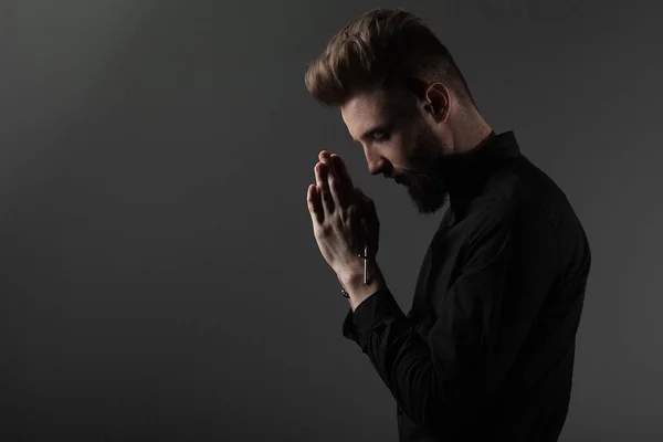 El sacerdote con las manos dobladas con una cruz en la cabeza reza con los ojos cerrados sobre un fondo gris — Foto de Stock