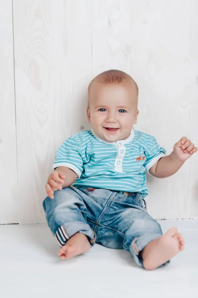 Bebé es muy lindo sonriendo sentado en el suelo contra un fondo claro — Foto de Stock
