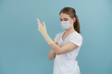 Maskeli kadın doktor mavi arka planda lastik eldiven takıyor.
