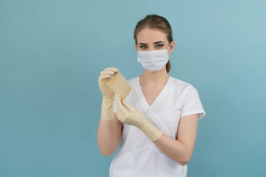 Doktorun elinde mavi arka planda eldiven ve maskeyle yanmış tıbbi bir yara bandı var.