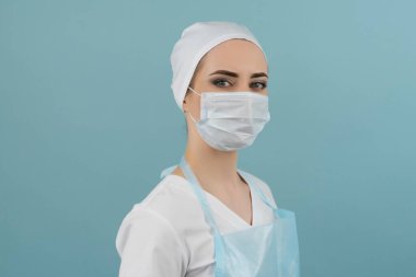 Önlüklü maskeli doktor ve eldivenler mavi arka planda ameliyata hazırlanıyor.