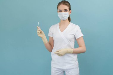 Maskeli ve eldivenli doktor mavi arka plandaki bir damlaya kateter takıyor.