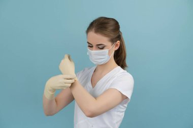 Maskeli kadın doktor mavi arka planda lastik eldiven takıyor.