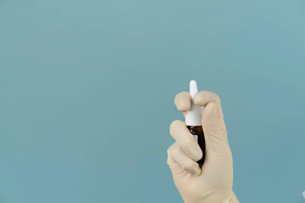 Maskeli doktor mavi arka planda elinde sprey tutuyor.