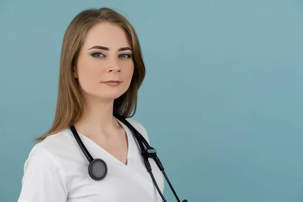 Beyaz kadın doktor kameraya bakıyor boynunda steteskopla mavi arka planda.