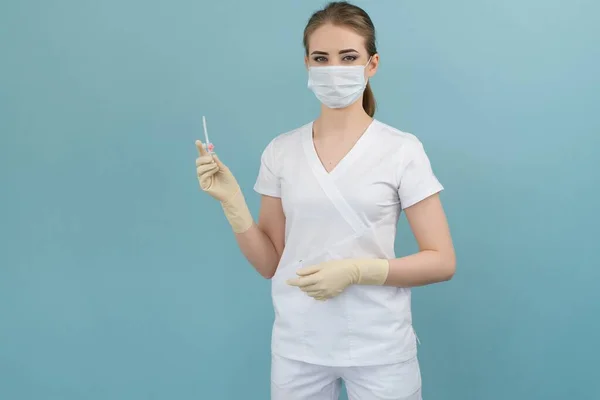 Maskeli ve eldivenli doktor mavi arka plandaki bir damlaya kateter takıyor.
