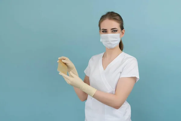 Doktorun elinde mavi arka planda eldiven ve maskeyle yanmış tıbbi bir yara bandı var.
