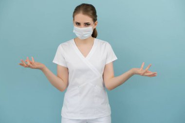 Maskeli kadın doktor mavi bir arka planda endişe ve korku gösteriyor.