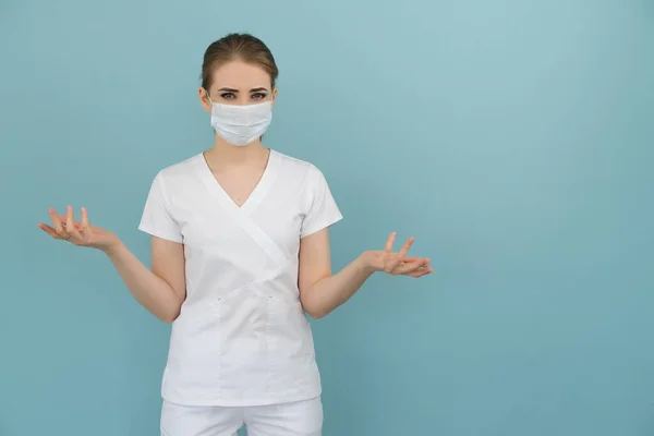 Vrouwelijke arts in een masker toont angst en angst met handen op een blauwe achtergrond — Stockfoto