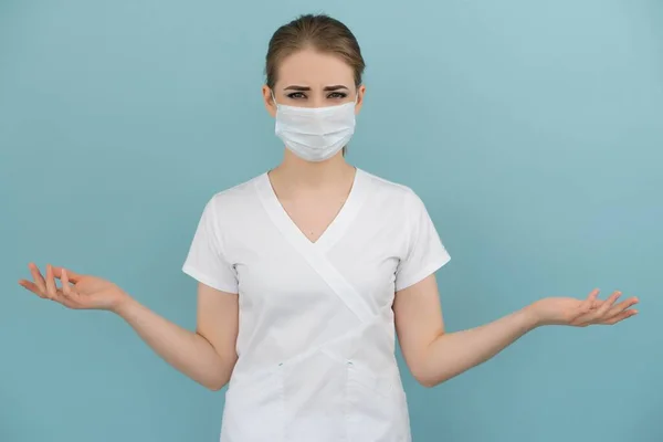 Maskeli kadın doktor mavi bir arka planda endişe ve korku gösteriyor.