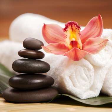 Spa arka planı. Egzotik bitkiler üzerinde beyaz havlular, güzel orkide çiçekleri ve rahatlatıcı spa masajı ve vücut bakımı için dengeleyici taşlar. Aromalı Asya ilaçları ve sağlıklı vücut için taş terapisi.