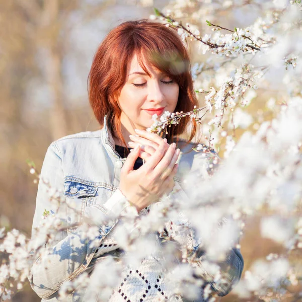 Beautiful young woman enjoying of the spring blooming. Outdoor lifestyle. Happy smiling woman enjoying a smell of flowers in spring garden — Stock Photo, Image