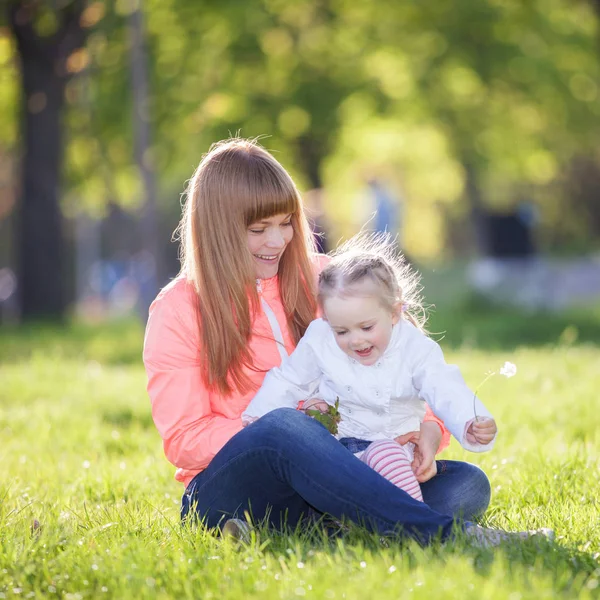 母亲和女儿在公园里。美自然场景丰富多彩的背景，在春暖花开的季节。家庭的户外生活方式。幸福的女人，可爱的女孩在绿色草地上放松 — 图库照片