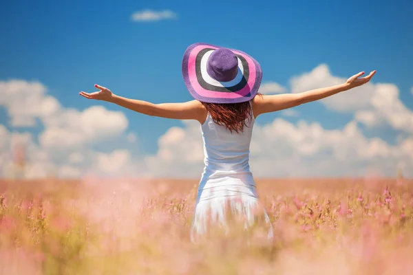 Heureuse femme qui embrasse la vie dans les champs avec des fleurs. Beauté de la nature, ciel nuageux bleu et champ coloré avec des fleurs. Style de vie extérieur. Concept de liberté. Femme dans le champ d'été — Photo