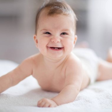 Eğlenceli portresi yakın bebek. Gülen bebek beyaz güneşli yatak odasında. Aile sabah evde. Çocuk beyaz yatakta rahatlatıcı. Tekstil ve çocuklar için yatak. Kameraya bakarak çocuğun