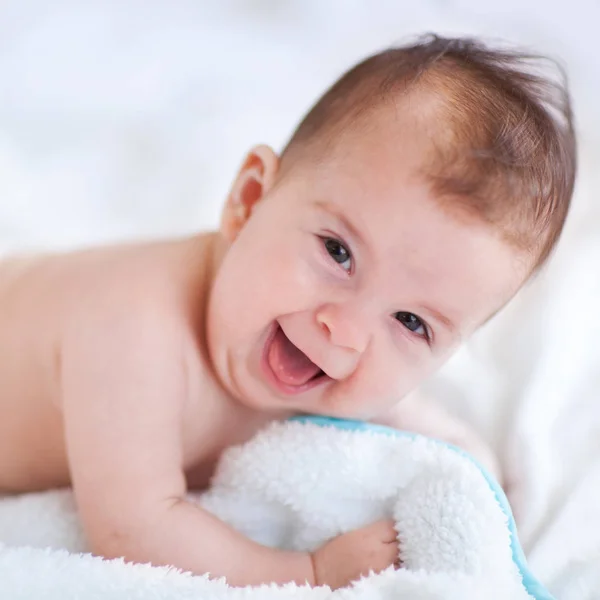 Feche o retrato do bebê divertido. Laughing bebê no quarto ensolarado branco. Manhã de família em casa. Criança relaxante na cama branca. Têxtil e roupa de cama para crianças. Miúdo a olhar para a câmara — Fotografia de Stock