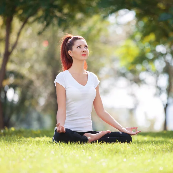 Mooie vrouw doen yoga oefeningen in het park. Schoonheid natuur scène met kleurrijke achtergrond op lente seizoen. Outdoor lifestyle. Gelukkige vrouw ontspannen op groen gras — Stockfoto