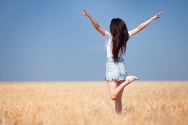 Mutlu kadın tarladaki hayatın tadını çıkarıyor doğa güzelliği, mavi gökyüzü ve altın buğdaylı tarla. Açık hava yaşam tarzı. Özgürlük kavramı. Yaz tarlasında atlayan kadın
