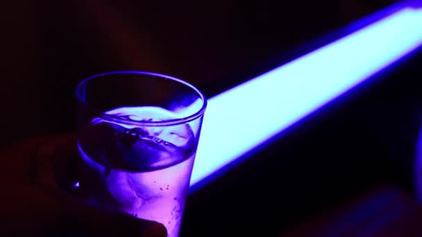 A bottle glass of soda water with neon light closeup handheld — ストック動画