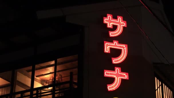 Een neon boord door japanese voorganger 's nachts handheld lage hoek — Stockvideo