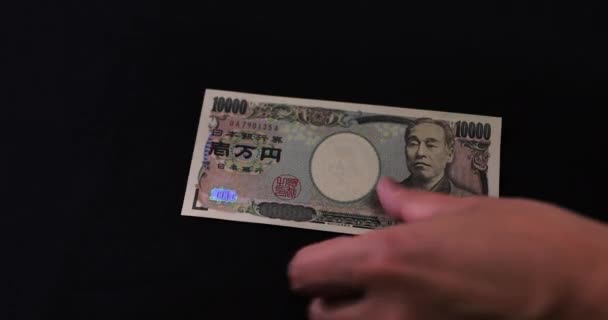 Contando la moneda japonesa 100.000 yenes a mano sobre el fondo negro — Vídeos de Stock