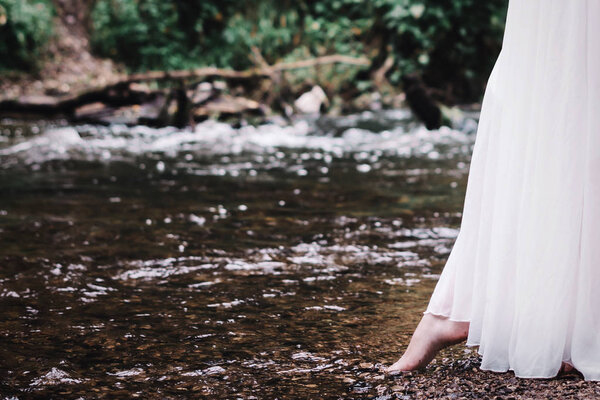 A beautiful girl in a white dress is walking along the river.
