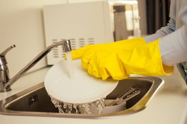 Mutsuz kızıl saçlı güzel kadın sarı eldiven giyiyor ve kirli bulaşık yığınlarını yıkıyor. Bardaklar, tavalar, mutfaktaki tencereler.