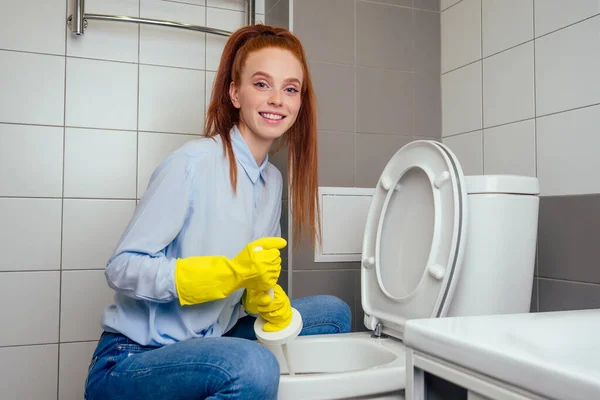 Весела руда імбирна жінка миє в туалеті в рукавичках — стокове фото