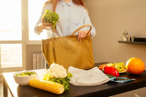 Mujer de jengibre repelente ecológica que clasifica las compras de la cocina de algodón eco bolsa de sol puesta de sol fondo. Ningún paquete de plástico verde paz. —  Fotos de Stock