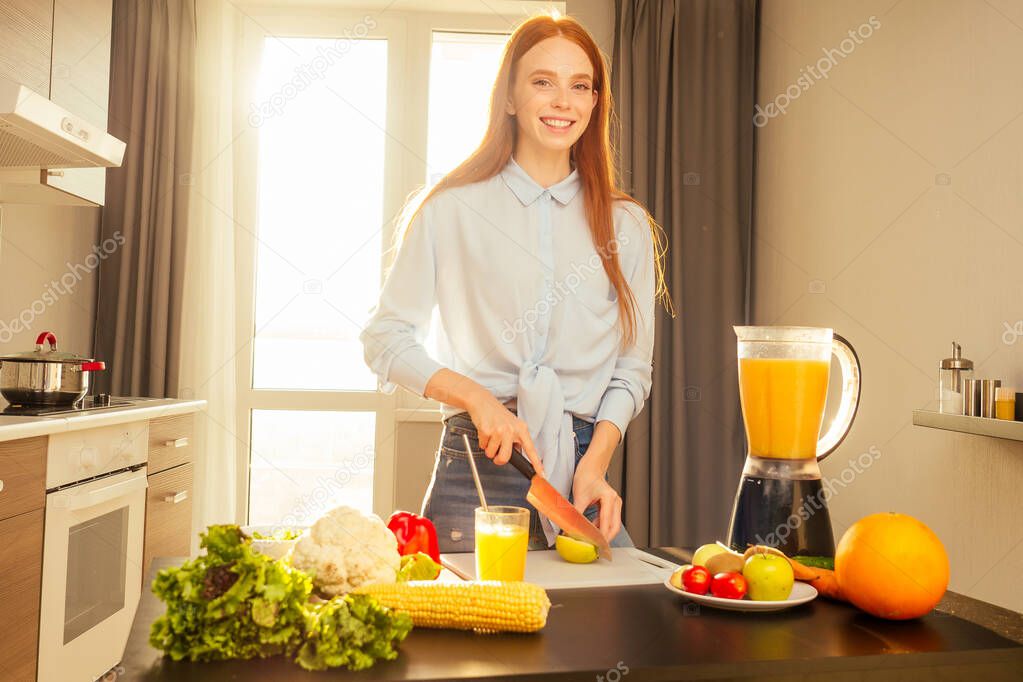 happy redhaired ginger woman cooking smoothie from apple in evening sun lights sunset background