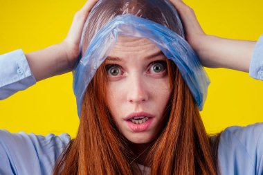 Güzel kızıl saçlı, kızıl saçlı, stil sahibi bir kadın kafasına kırmızı plastik polietilen bir paket ve sarı arka planda güneş gözlüğü takıyor. Hızlı moda problemi kavramı.